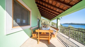Ein Balkon mit Holztisch und Stühlen, Blick aufs Meer und eine grüne Gebäudefassade.