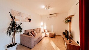 Un salon avec un canapé, une plante en pot, des œuvres d’art accrochées au mur et un téléviseur.