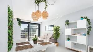 Una sala de estar moderna con comedor, muebles blancos y plantas verdes.