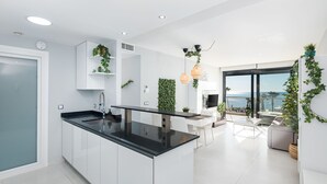 Una cocina moderna con una isla central, armarios blancos y vistas al mar.