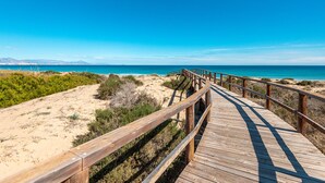 Un muelle de madera que lleva a una playa con cielos despejados y montañas a lo lejos.