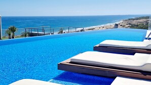 Una piscina con vista al océano, sillas de descanso y una terraza.