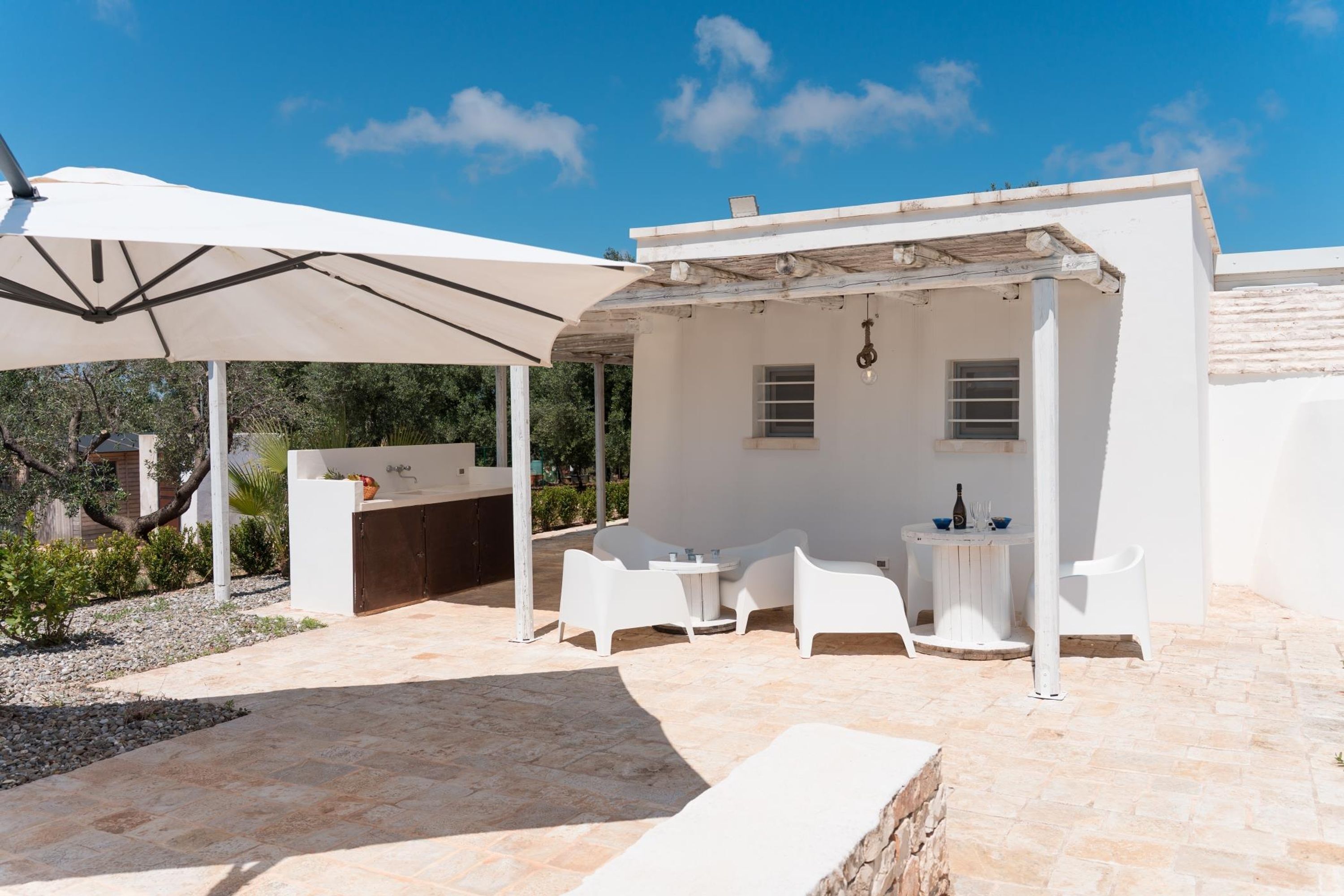 An outdoor patio with a white umbrella, a barbecue area, and white furniture.