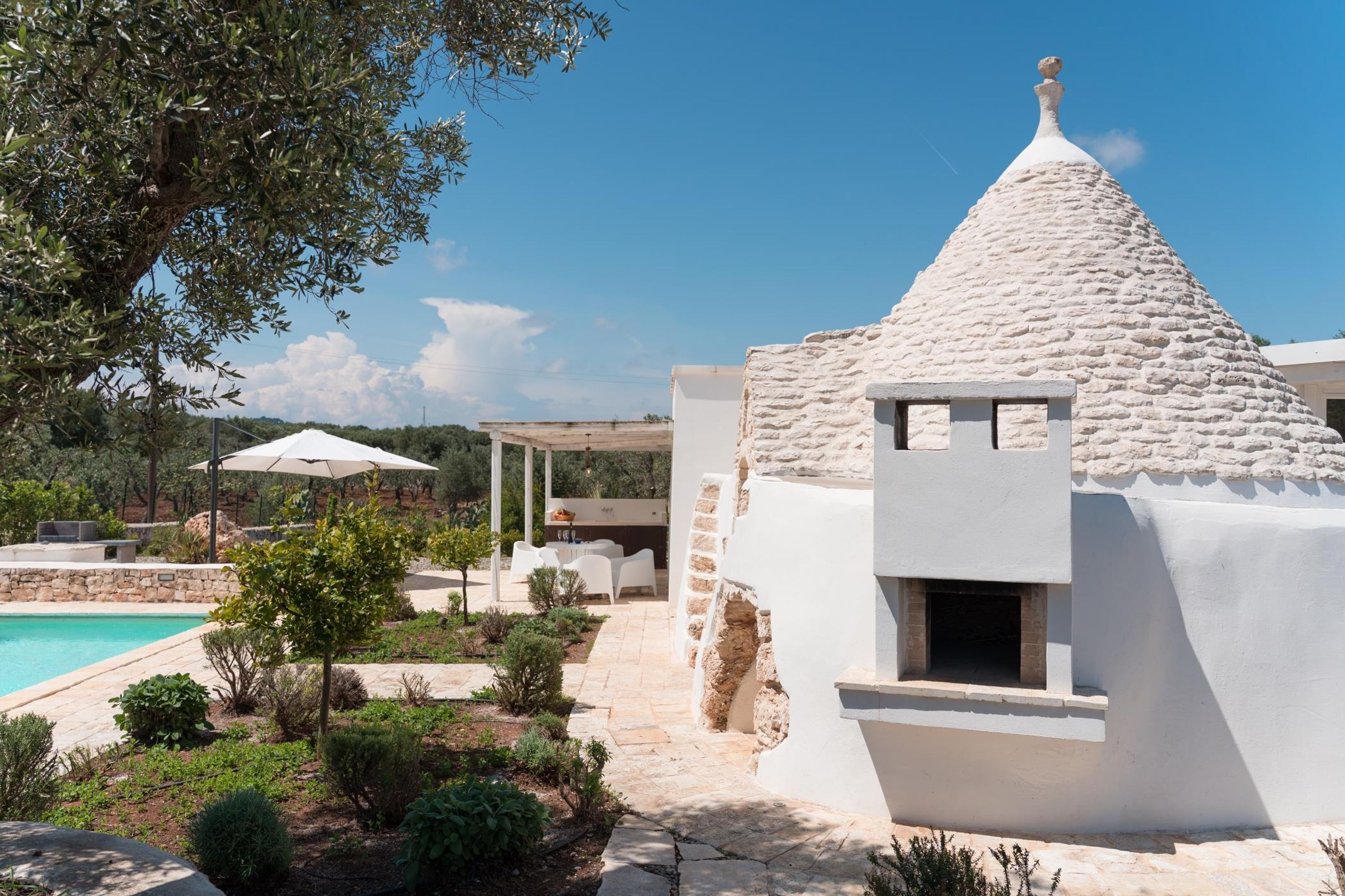 A white villa with a stone roof, a swimming pool, and a patio area with outdoor furniture.