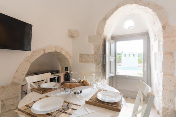 Un comedor con un arco de piedra, una mesa dispuesta con platos, vasos y cubiertos, y un televisor montado en la pared.
