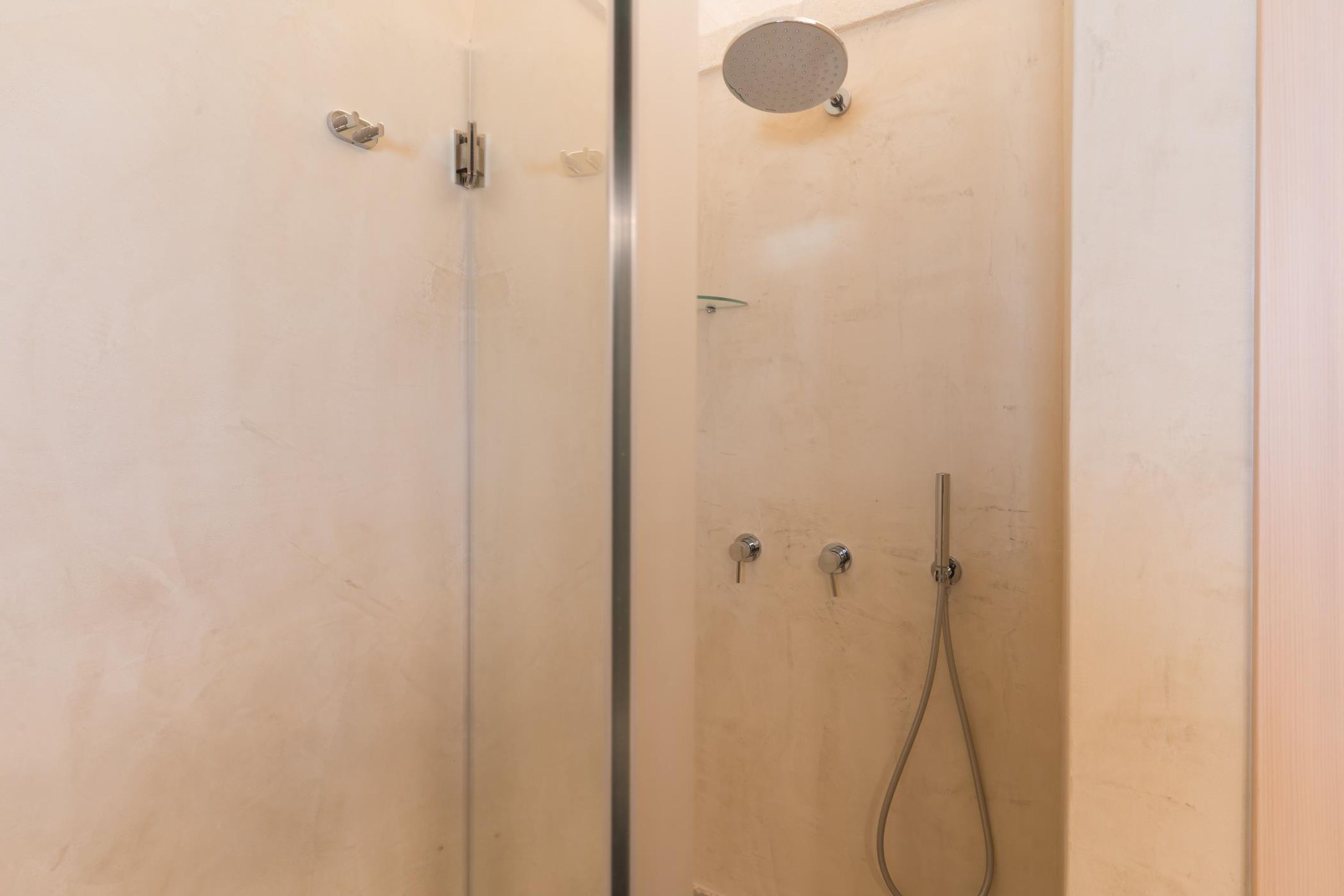 A glass-enclosed shower with a handheld showerhead and a wall-mounted faucet.