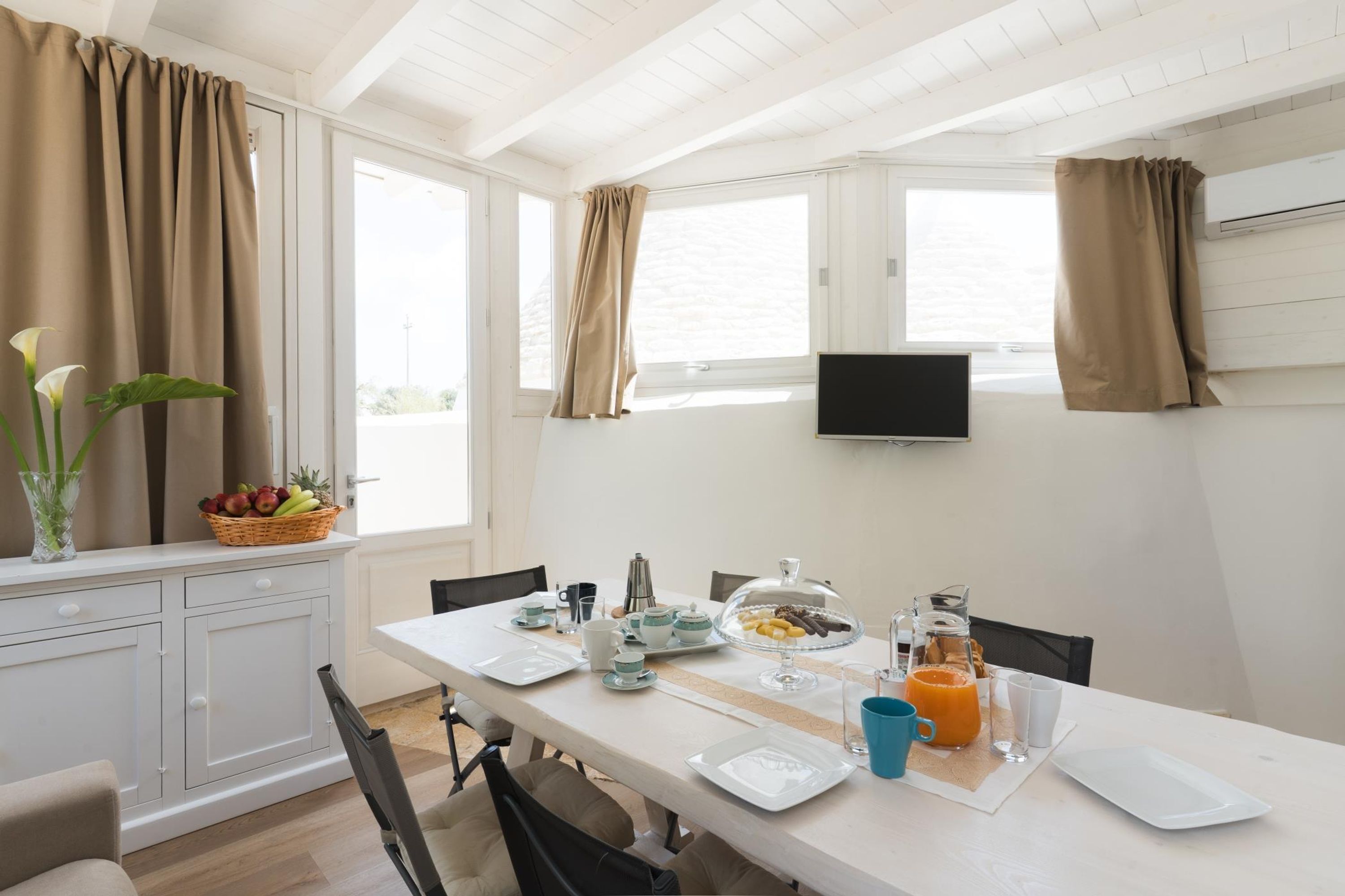 A dining area with a table set for breakfast, including plates, cups, and a fruit basket.