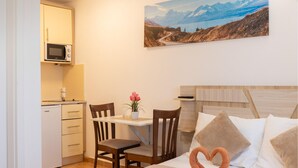 Ein Schlafzimmer mit Bett, Schreibtisch, Stuhl, einer Mikrowelle und einem Gemälde von einer Berglandschaft.