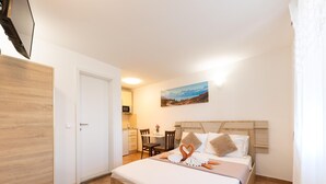 Ein Hotelzimmer mit einem Bett, einem Schreibtisch und einem Stuhl. An der Wand hängt ein Gemälde und links befindet sich eine Tür.