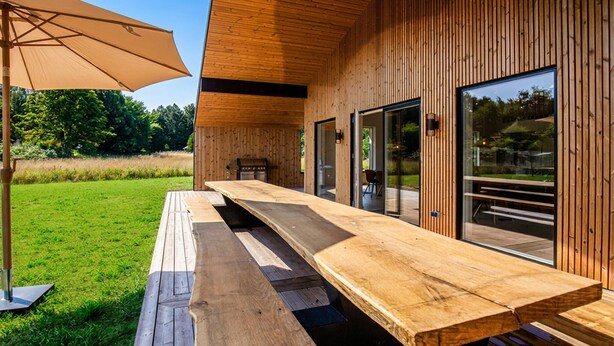 A wooden deck with a long table and benches, surrounded by glass doors and windows.