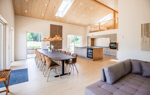 Un vaste espace de vie comprenant une salle à manger avec table, des canapés et une cuisine équipée d’appareils électroménagers modernes.