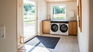 A laundry room with a washing machine, dryer, and a window providing a view of greenery outside.