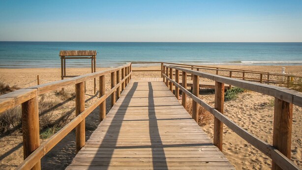 A wooden boardwalk leading to a beach with a bench and a clear view of the ocean. - Beautiful apartment in Santa Pola with WiFi (Santa Pola)