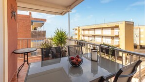 A balcony with a glass table, chairs, and a bowl of fruit. There are potted plants and a view of buildings in the background. - Beautiful apartment in Santa Pola with WiFi (Santa Pola)