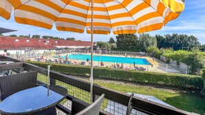 Un espace piscine agrémenté d’un grand parasol à rayures, d’une table de billard et offrant une vue sur la piscine.