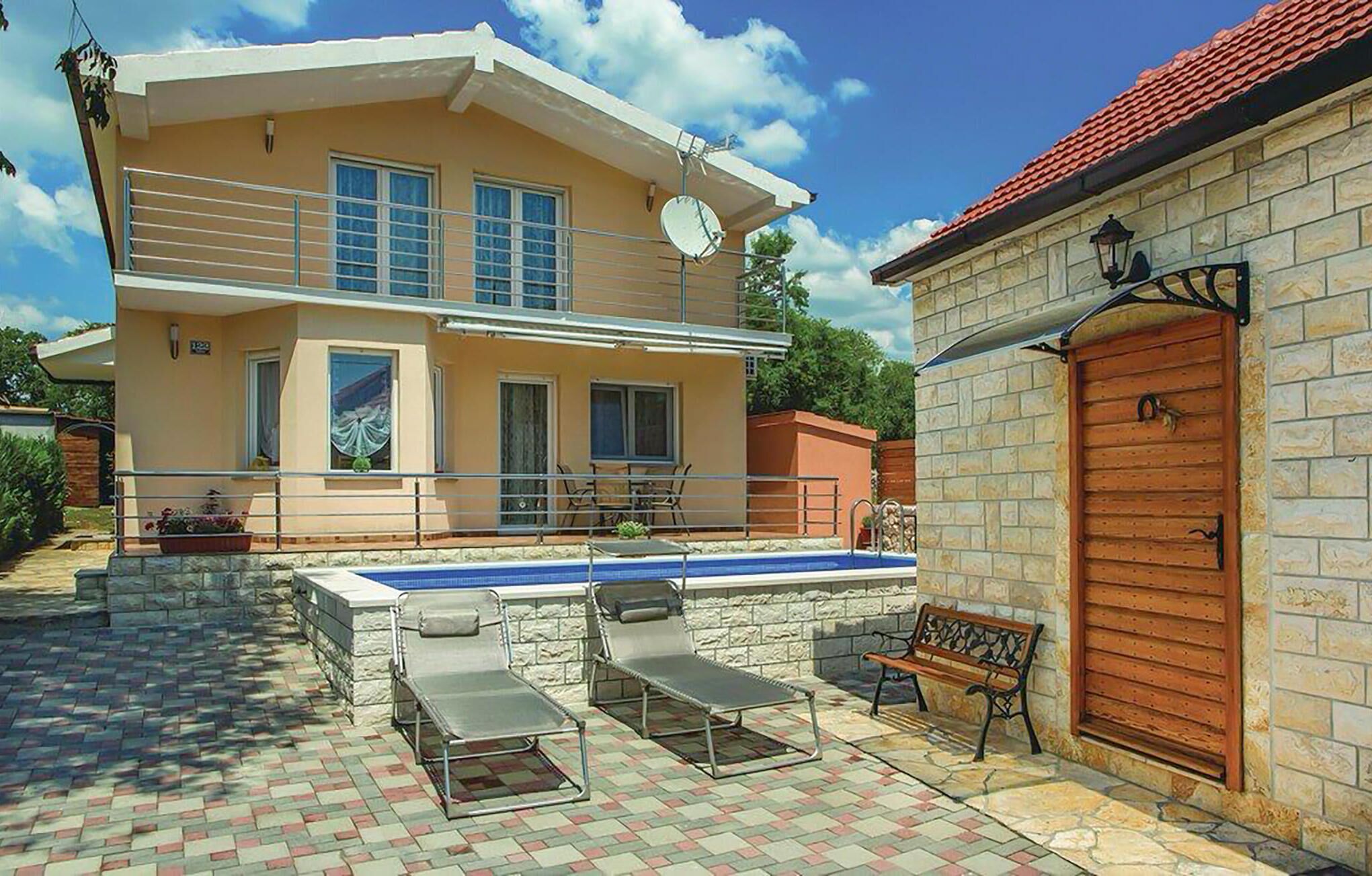 Uma casa de dois andares com piscina, área de estar externa e um muro de pedra.