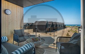 A balcony with wicker furniture, a round table with fruits and a bottle, and a view of a coastal building complex. - Havnehusene, Lejl. 36 (Slagelse)