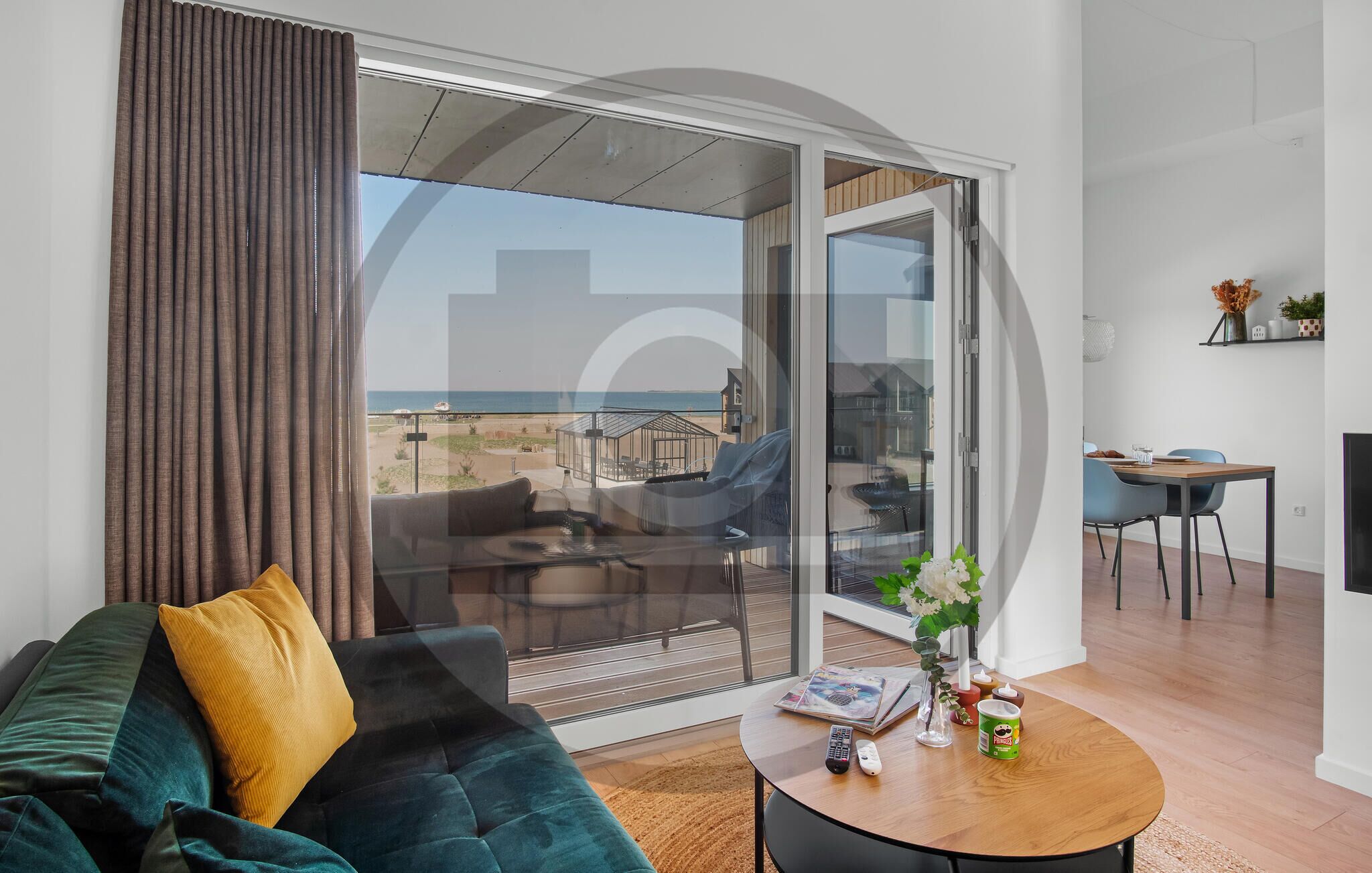 A modern living room with a sofa, a coffee table, and a view of the beach through large glass doors.