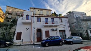 Un edificio de dos pisos con fachada blanca, un arco de entrada central y un balcón en el nivel superior.