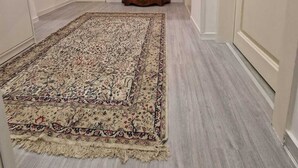 Un pasillo con un tapete grande de estampado llamativo, un mueble de madera con un espejo y una lámpara, y una puerta.