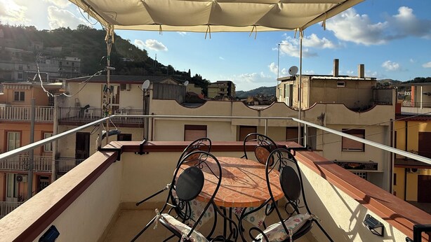 Una terraza en la azotea con mesa y sillas, un toldo protector y vistas de los edificios circundantes.