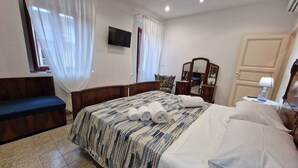 Una habitación de hotel con una cama, un banco, un aparador, un espejo y un televisor en la pared.