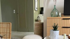 A room with a wicker chair, a round white pouf, a small round table with a white candle, a vase with dried pampas grass, and a cabinet with a plant. - Double room with private bathroom (Senlis)