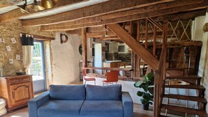 Un interior rústico con una escalera de madera, un sofá y una cocina al fondo.