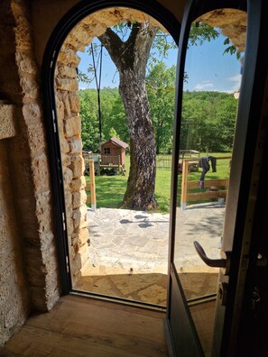An arched doorway leading to a stone-paved area with a wooden deck and a small wooden structure.