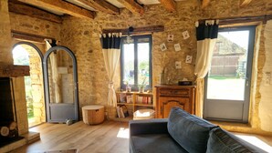 Una habitación rústica con pared de piedra, vigas de madera, un sofá, un espejo y una ventana con cortinas.
