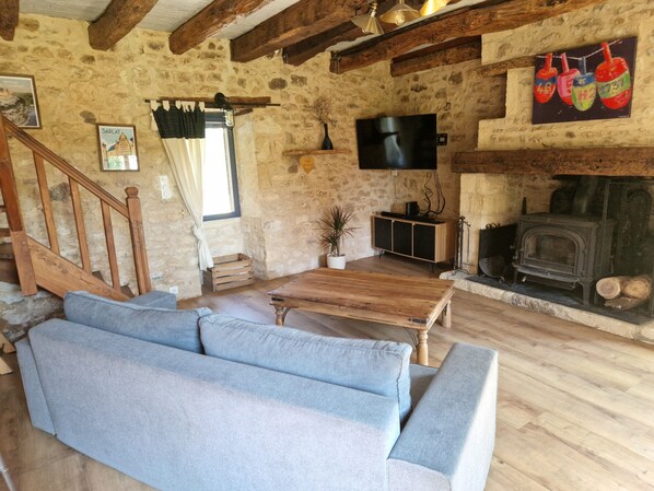 A rustic living room with a stone wall, wooden beams, a sofa, a TV, and a fireplace.