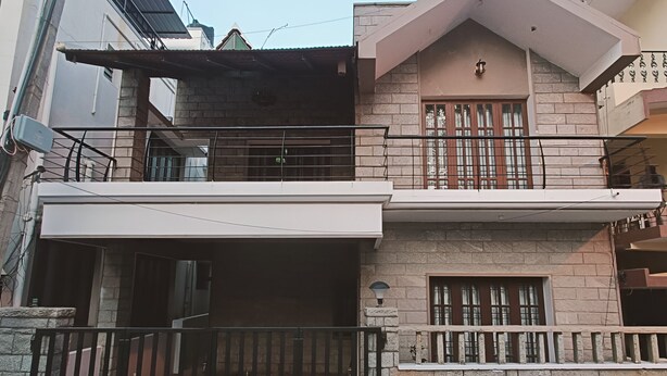 Una casa de dos pisos con balcón, entrada protegida por un portón y una ventana pequeña.