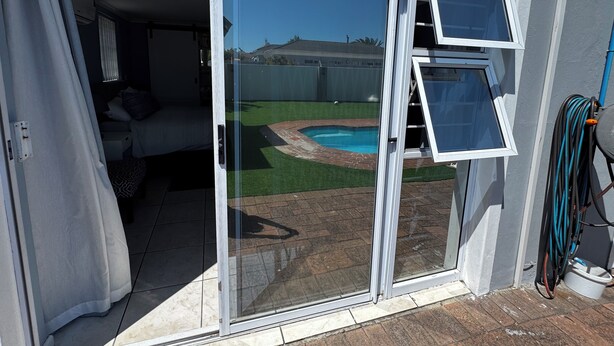A sliding glass door leading to a backyard with a swimming pool and a grassy area. - Cosy space for work or getaway close to Blougberg beach Cape Town (Cape Town)