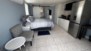 A compact hotel room with a bed, bedside table, chair, and a kitchenette area including a refrigerator and sink. - Cosy space for work or getaway close to Blougberg beach Cape Town (Cape Town)