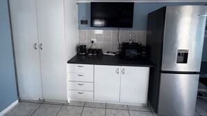 A compact kitchen with white cabinets, a black countertop, a stainless steel refrigerator, a microwave, a kettle, and a flat-screen TV mounted above the counter. - Cosy space for work or getaway close to Blougberg beach Cape Town (Cape Town)