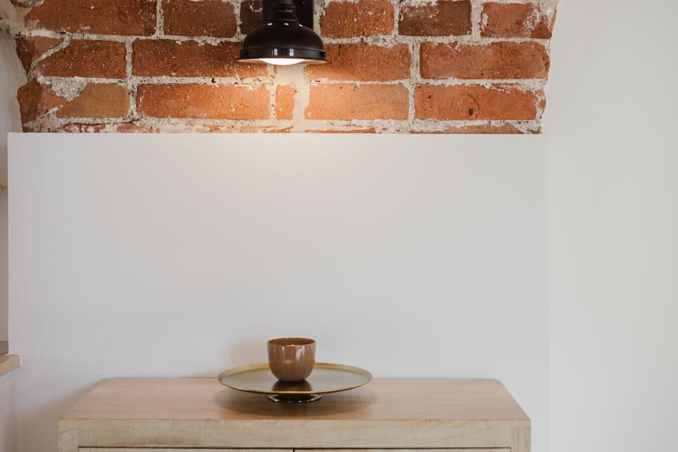 Un mur de briques surmonté d’un luminaire suspendu noir, au-dessus d’une table en bois dont le plateau est en verre.