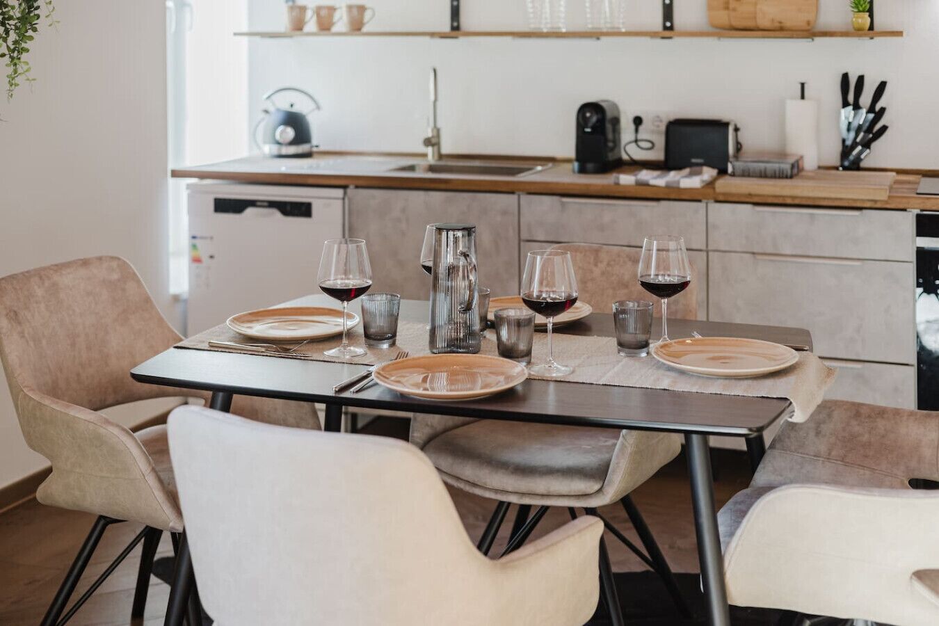 Een eettafel gedekt met borden, glazen en bestek, met een keuken op de achtergrond.