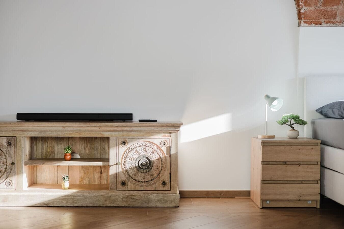 Ein schlicht eingerichteter Raum mit einem Holzschrank, einem kleinen Nachttisch mit Lampe und einem Bett.