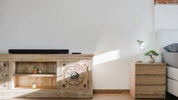 Ein schlicht eingerichteter Raum mit einem Holzschrank, einem kleinen Nachttisch mit Lampe und einem Bett.