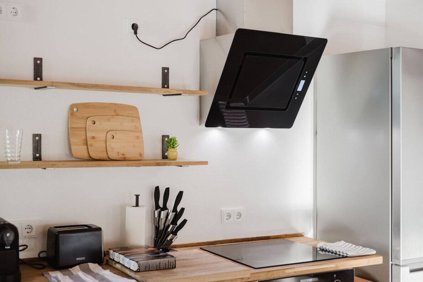 A modern kitchen with wooden shelves, a cutting board, a toaster, and a knife block.