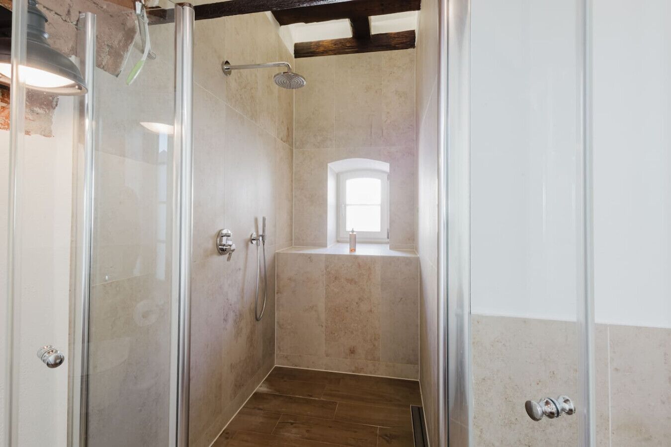 Ein Badezimmer mit Dusche, Fenster und Holzboden.