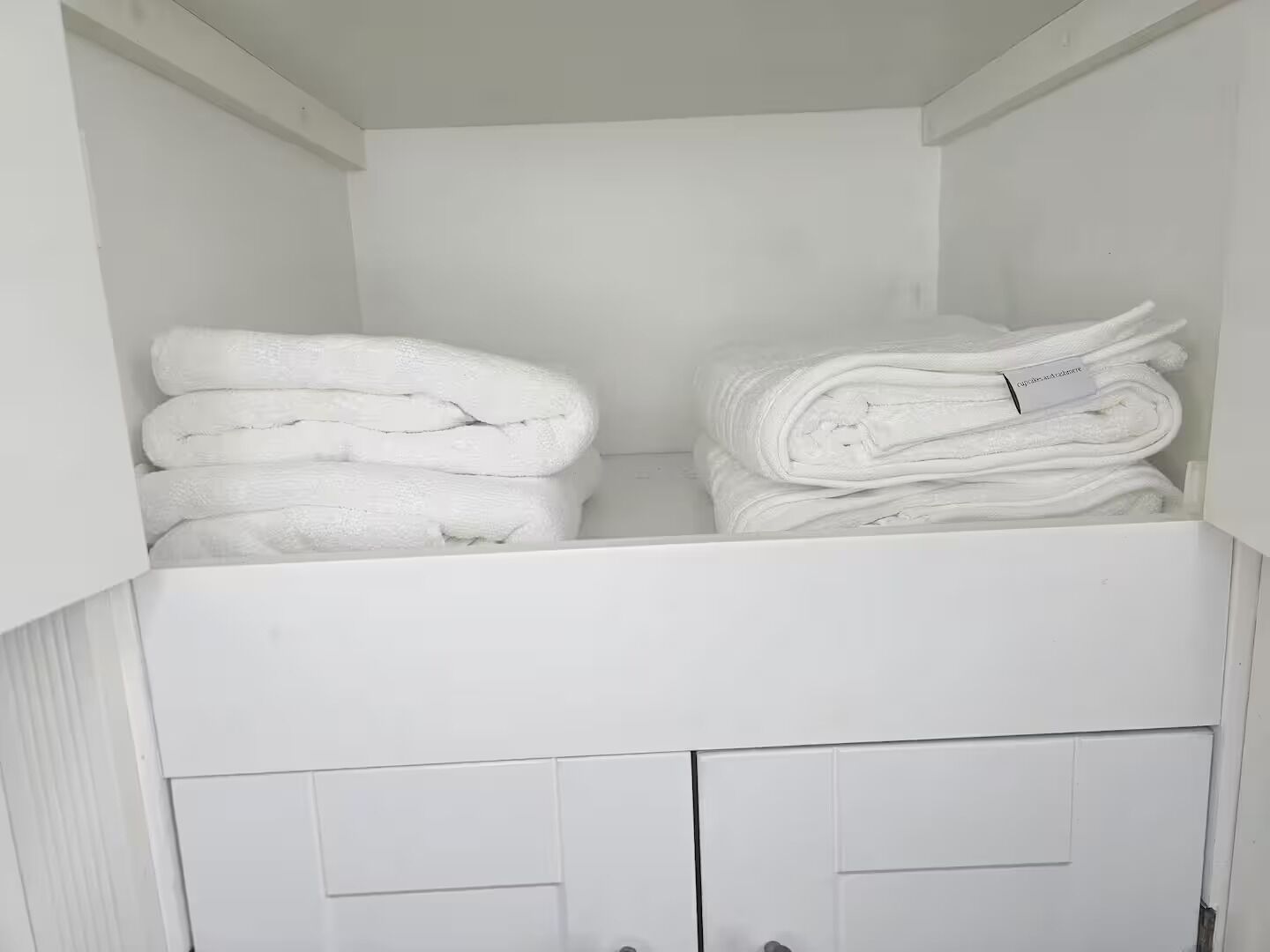 A white storage unit with two shelves, each holding neatly folded white towels.