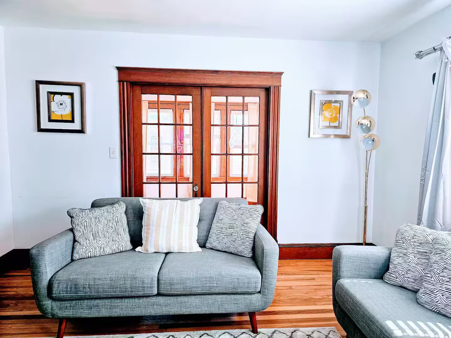 A living room with a grey sofa, patterned cushions, a wooden door, and a floor lamp.
