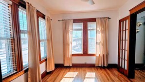 Une pièce dotée d’un plancher en bois, de grandes fenêtres avec des rideaux et d’un ventilateur de plafond.