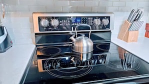 Une cuisine avec un four à plaques de cuisson noires, une bouilloire sur le réchaud et un bloc à couteaux sur le plan de travail.