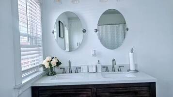 A bathroom with two sinks, a large mirror, and a window with blinds.