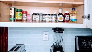 Une cuisine avec un plan de travail blanc, un mixeur et divers épices et condiments.