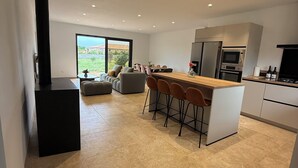 A modern kitchen with a central island, bar stools, and a large window offering a view of the outdoors. - Air-conditioned house, South Corsica, 4 bedrooms, 2 bathrooms, 15 min from the beach (Figari)
