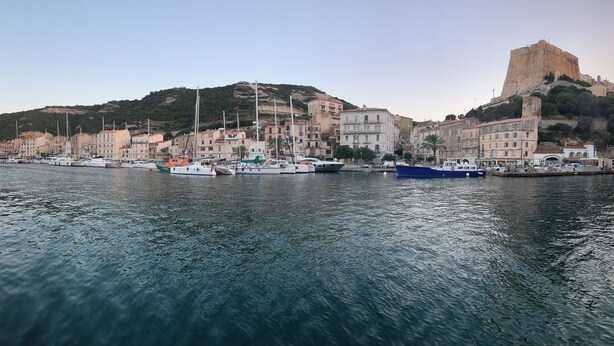 A harbor with boats docked, buildings along the waterfront, and a prominent hill with a fort-like structure. - Air-conditioned house, South Corsica, 4 bedrooms, 2 bathrooms, 15 min from the beach (Figari)