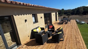 A wooden deck with outdoor furniture, a covered patio area, and a view of a forested hill. - Air-conditioned house, South Corsica, 4 bedrooms, 2 bathrooms, 15 min from the beach (Figari)